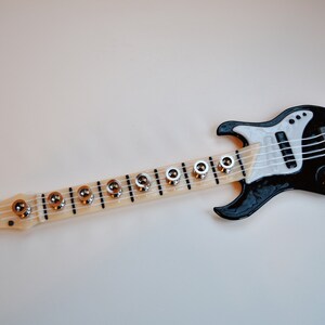 May include: A black and white toy electric guitar with a long neck and silver tuning pegs.