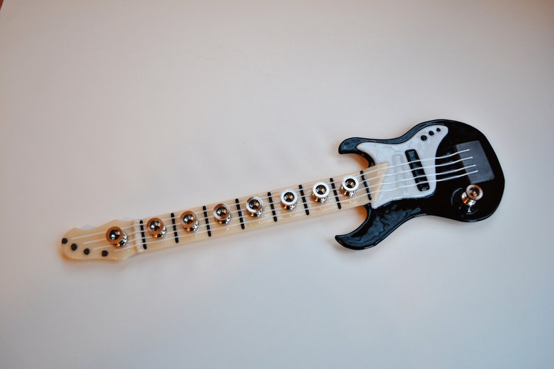 May include: A black and white toy electric guitar with a long neck and silver tuning pegs.