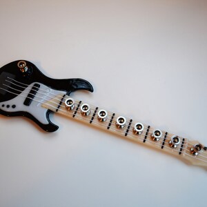 May include: A black and white miniature electric bass guitar with a wooden neck and silver tuning pegs.