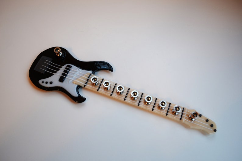 May include: A black and white miniature electric bass guitar with a wooden neck and silver tuning pegs.