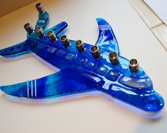 May include: A blue glass menorah shaped like an airplane with white stripes on the wings. The menorah has nine candle holders.