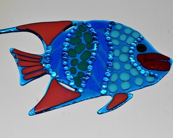 May include: A blue and red glass fish with green and white accents. The fish has a rounded body and a long, thin tail. It is decorated with small, round dots and a pattern of green and white circles.