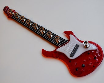 May include: A red electric guitar with a white pickguard and black and white striped fretboard. The guitar has a unique, angular shape and is made of glass.