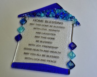 Könnte beinhalten: Ein blauer gläserner Haus-Anhänger mit weißem Hintergrund und blauen und türkisfarbenen Glasperlen. Der Anhänger hat eine gedruckte Botschaft, die lautet: "HOME BLESSING MAY THIS HOME BE BLESSED WITH LOVE, WARMTH AND LAUGHTER MAY THIS HOME BE BLESSED WITH JOY, FRIENDSHIP GOOD HEALTH AND WEALTH MAY YOU ALL BE BLESSED WITH LUCK AND PEACE"