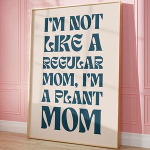 Op de afbeelding: Een ingelijst print met een witte achtergrond en een gouden lijst. De tekst op de print luidt "I'm not like a regular mom, I'm a plant mom" in een blauw lettertype.