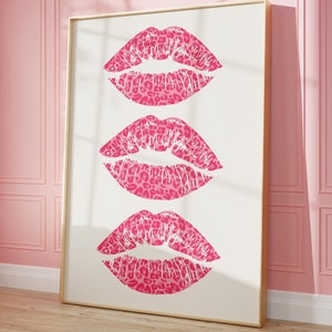 Framed wall art print featuring three pink lips with a leopard print design, arranged vertically on a white background, leaning against a pink paneled wall in a well-lit room.