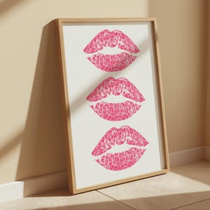 Framed wall art print featuring three pink lips with a leopard print design, arranged vertically on a white background, leaning against a pink paneled wall in a well-lit room.