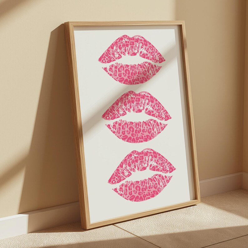 Framed wall art print featuring three pink lips with a leopard print design, arranged vertically on a white background, leaning against a pink paneled wall in a well-lit room.