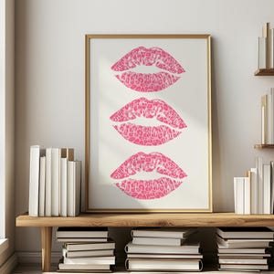 Framed wall art print featuring three pink lips with a leopard print design, arranged vertically on a white background, leaning against a pink paneled wall in a well-lit room.