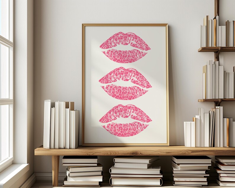 Framed wall art print featuring three pink lips with a leopard print design, arranged vertically on a white background, leaning against a pink paneled wall in a well-lit room.