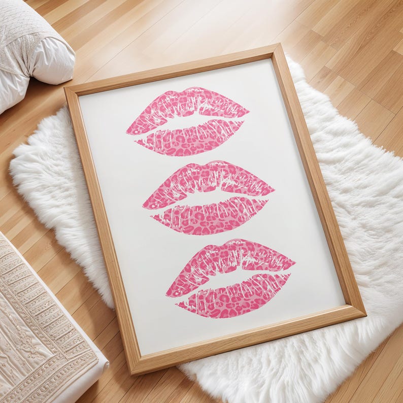 Framed wall art print featuring three pink lips with a leopard print design, arranged vertically on a white background, leaning against a pink paneled wall in a well-lit room.
