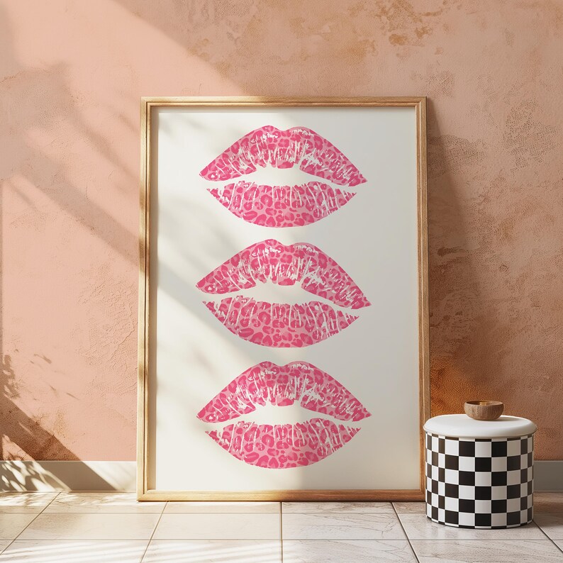 Framed wall art print featuring three pink lips with a leopard print design, arranged vertically on a white background, leaning against a pink paneled wall in a well-lit room.