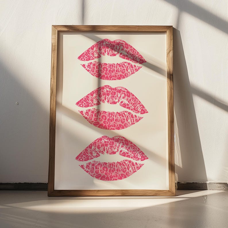 Framed wall art print featuring three pink lips with a leopard print design, arranged vertically on a white background, leaning against a pink paneled wall in a well-lit room.
