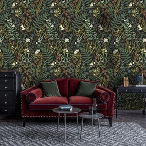 May include: A red velvet sofa with green throw pillows sits in front of a dark green wallpaper with a floral pattern. A black dresser and a black side table with two drawers are also in the room.
