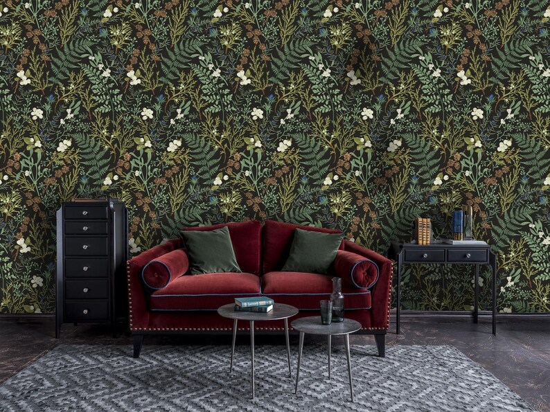 May include: A red velvet sofa with green throw pillows sits in front of a dark green wallpaper with a floral pattern. A black dresser and a black side table with two drawers are also in the room.