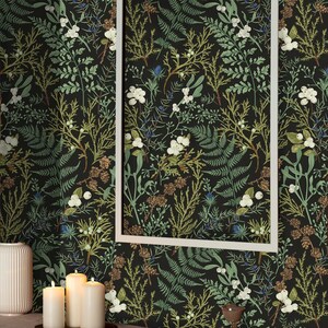 May include: A black and green wallpaper with a botanical pattern featuring ferns, leaves, and white flowers. The wallpaper is framed by a white picture frame and displayed on a wall in a room with a table and candles.
