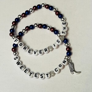 May include: Two beaded bracelets with silver and blue beads. One bracelet spells "FOREVER IS THE" and the other spells "SWEETEST CON" with a silver boot charm.
