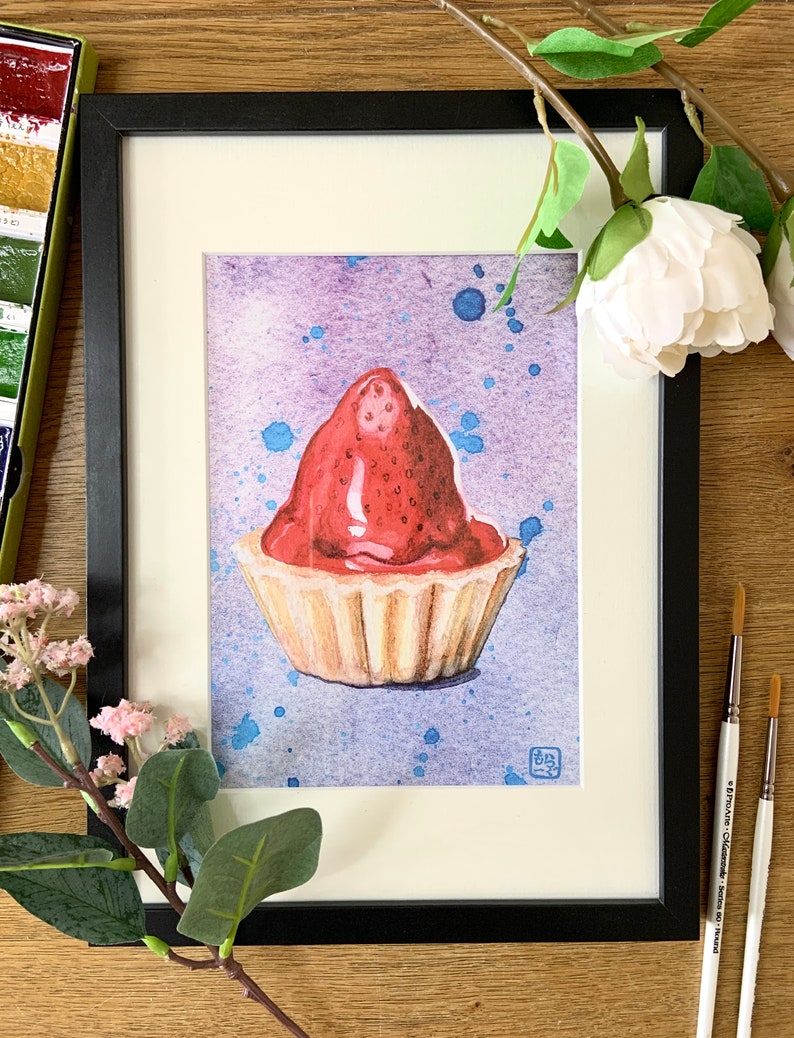 Framed watercolour print of a Scottish strawberry tart on a splattered purple and blue background, on a wooden table surrounded by paintbrushes and flowers