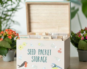 May include: A light beige wooden seed packet storage box with an open lid. The box is decorated with illustrations of a robin and a blue tit, and the words "SEED PACKET STORAGE". Inside are labeled dividers for different seed types. The box is ideal for garden enthusiasts.