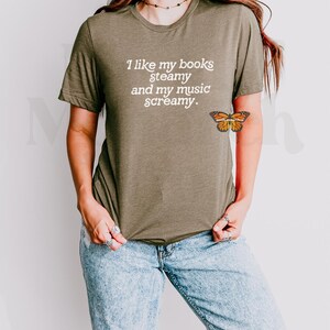 May include: A woman wearing a green t-shirt with the text "I like my books steamy and my music screamy."  She is wearing blue jeans and has a butterfly tattoo on her arm.