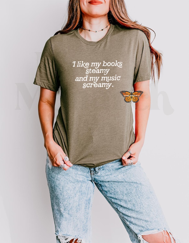 May include: A woman wearing a green t-shirt with the text "I like my books steamy and my music screamy."  She is wearing blue jeans and has a butterfly tattoo on her arm.