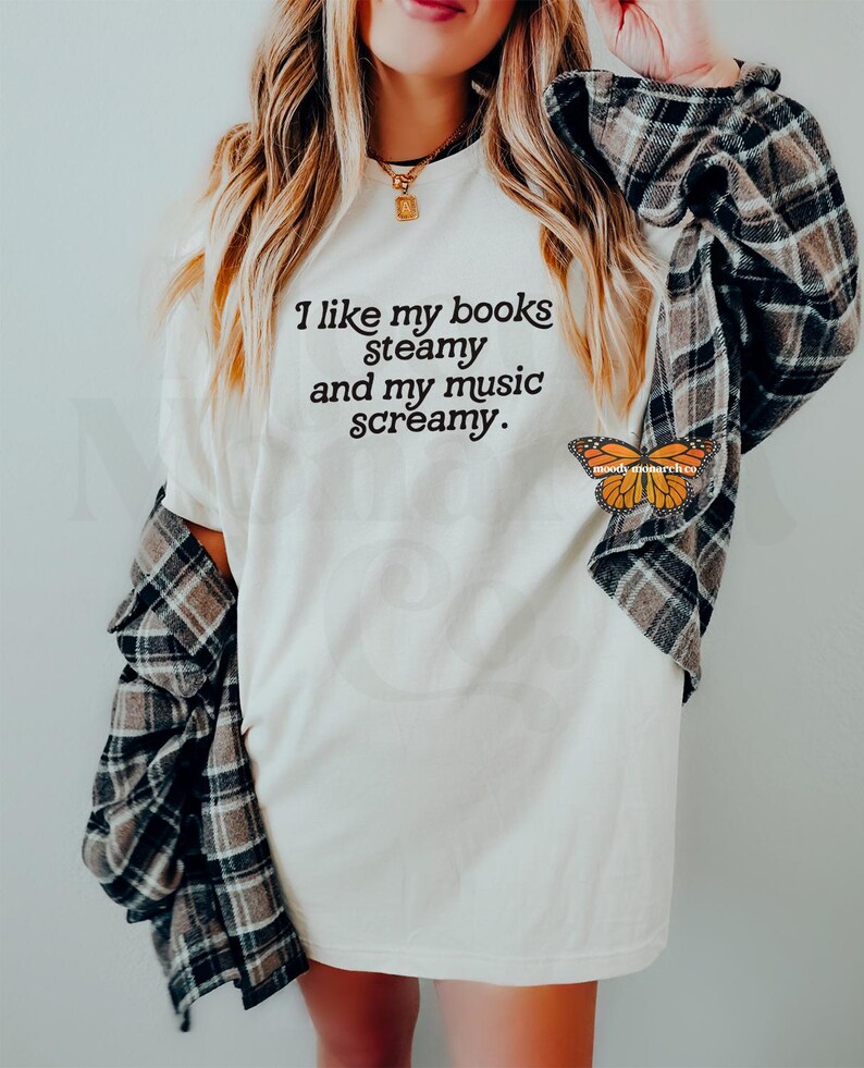 May include: White t-shirt with the text "I like my books steamy and my music screamy." printed in black. A butterfly sticker is on the bottom right corner of the shirt.