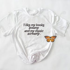 May include: White t-shirt with the text "I like my books steamy and my music screamy."
