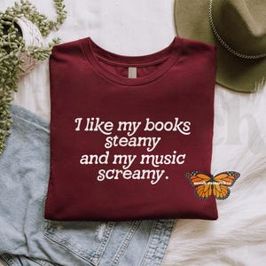 May include: A maroon t-shirt with the text "I like my books steamy and my music screamy." printed in white.