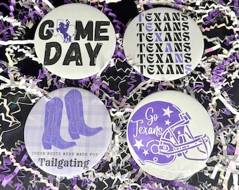May include: Four round buttons with white backgrounds and purple designs. One says "GAME DAY" with a silhouette of a person on a horse. Another says "TEXANS" multiple times. A third has purple cowboy boots and says "THESE BOOTS WERE MADE FOR TAILGATING". The last says "Go Texans" with a football helmet.