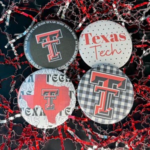 May include: Four round buttons with Texas Tech University designs. One button is black with a red and white "T" logo and "Texas Tech" text. Another is white with red text and polka dots. The other two buttons have the "T" logo on a red Texas outline and a black and white checkered pattern.
