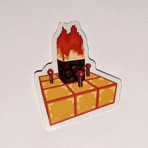 May include: A sticker featuring a pixelated design of a structure with a fiery top, a dark brown center, and a golden base. Three red torches are placed around the structure. The sticker has a white border.