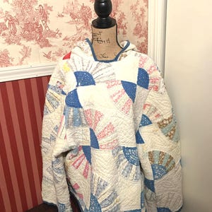 Op de afbeelding: Een vintage quilt met een blauw, wit en roze waaiervormig patroon. De quilt wordt getoond op een mannequin met een jute basis.