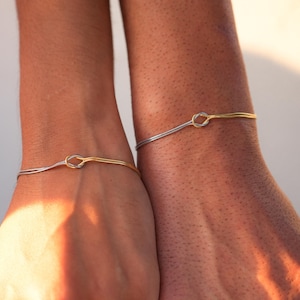 May include: Two matching bracelets with a knot design. One bracelet is silver and the other is gold.