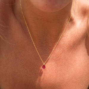 May include: A gold chain necklace with a small, teardrop-shaped red gemstone pendant.