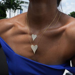 May include: A woman wearing a blue off-the-shoulder top with a gold chain necklace featuring two diamond-encrusted heart pendants.