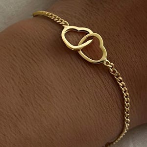 May include: A gold chain bracelet with two interlocking heart charms.