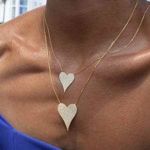 May include: A gold chain necklace with two heart-shaped pendants. Both pendants are covered in small, clear stones.