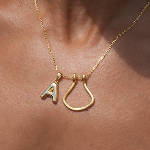 May include: A gold chain necklace with two charms: a letter 'A' and a teardrop-shaped pendant.