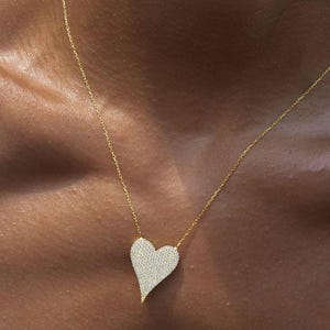 May include: A gold chain necklace with a large, heart-shaped pendant covered in sparkling clear stones.