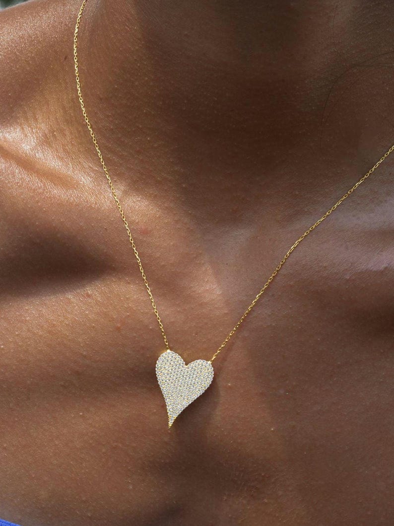 May include: A gold chain necklace with a large, heart-shaped pendant covered in sparkling clear stones.