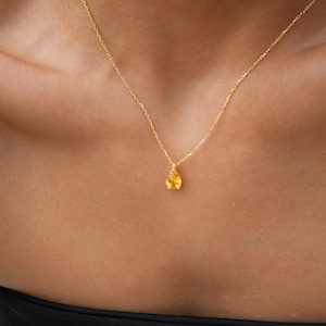 May include: A gold chain necklace with a small, teardrop-shaped yellow gemstone pendant.