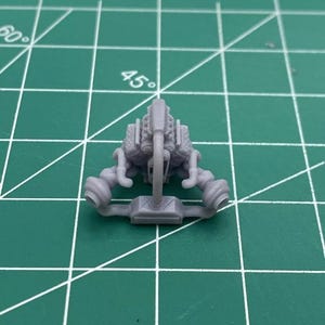 May include: A grey plastic model of a car engine with a detailed design. The engine has a large intake manifold and two exhaust manifolds.