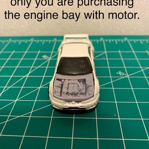 May include: A white toy car with the hood open, revealing a detailed engine bay. The text at the top of the image reads, "Car used for illustration only you are purchasing the engine bay with motor."