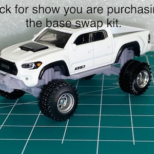 May include: A white Toyota Tacoma toy truck with large black off-road tires. The truck has a black hood vent and the text "Truck for show you are purchasing the base swap kit." is above the truck.