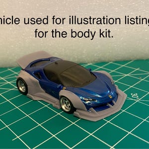 May include: A blue and gray toy car with a black roof and silver wheels sits on a green surface. The car has a spoiler and a front bumper. Text above the car reads: Vehicle used for illustration listing is for the body kit.