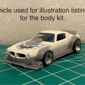 May include: A white and gray toy car with a custom body kit, featuring a hood scoop and a detailed front end. The car has a bird emblem on the hood and is set against a green grid background. Text on the image reads: Vehicle used for illustration listing is for the body kit.