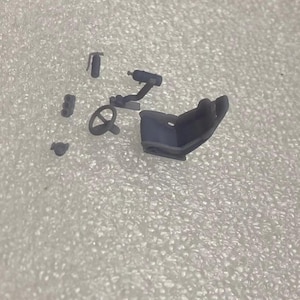 May include: A set of gray plastic model car interior parts, including a steering wheel, a seat, and a shifter. The parts are designed for a 1/24 scale model car.