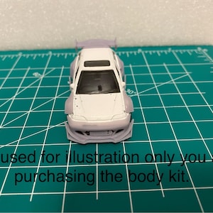 May include: A white model car with a custom body kit, including a spoiler and flared fenders. The car sits on a green cutting mat. Text on the mat reads "Car used for illustration only you are purchasing the body kit."