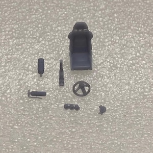 May include: A set of grey plastic model car parts, including a racing seat, steering wheel, exhaust pipes, and a fire extinguisher.