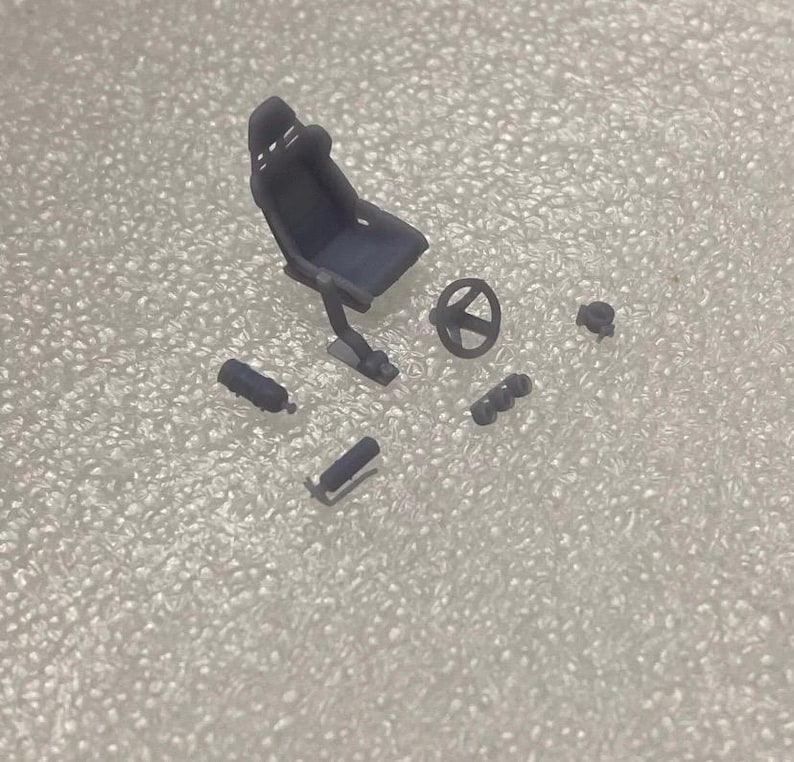 May include: A set of black plastic model car parts, including a racing seat, steering wheel, and various other accessories.